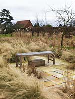 Midwinter grass beds with various miscanthus, Stipa tenuissima and Calamagrostis x acutiflora Overdam and Karl Foerster. Behind, orchard with trees and old chapel.