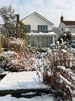 View to the house in a River Thames garden designed by Andy Sturgeon. Box topiary, grasses and architectural plants covered in snow.
