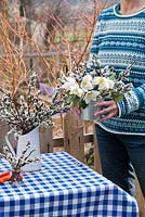 Woman making an arrangements with spring flowers - Christmas roses and catkins.