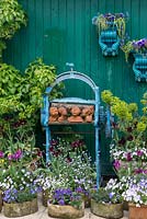 Clay heads on an old iron mangle painted blue forms a focal point in an arrangement of pots of violas, forget-me-nots and euphorbia, Tulipa 'Black Parrot' and 'Blue Parrot'.