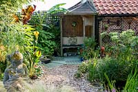 A town garden with covered seating area surrounded by tropical planting with Canna, Musa and Trachycarpus.