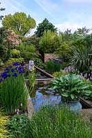 View along the pool, over lavender, potted hosta, Iris sibirica Caesar's Brother, Hakonechloa macra and pink Persicaria bistorta Superba and male ferns. Left border - photinia. Right border - phormium, Chusan Palm and maple. Pond sculpture by Peter Hayes.