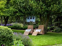 Wicker loungers in shade beneath a holly tree with the children's summer house beyond.