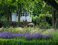 An elevated children's playhouse in a shady area with Hydrangea and Acanthus mollis. Box, lavender, Stipa tennuissima and Allium seedheads make up the foreground planting.