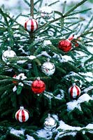 Outdoor Christmas tree with red and silver baubles, covered with snow