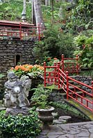Clivia miniata with Buddha statue in Oriental garden at Monte Palace Tropical Garden, Madeira, with red railings