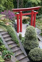 Oriental arch in garden at Monte Palace Tropical Garden, Madeira, with decorative urns, stone bridge, steps, cycads, bougainvillea, carex, and ferns