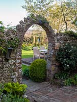 A stone arch provides the entrance to the rear of an English country garden in spring.