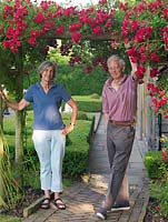 Anthony and Maggie McGrath beneath a pergola of Rosa Excelsa that leads to the Chequer Garden with its blocks of box, one room in their 3-acre country garden.
