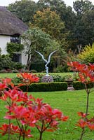 Seen over red foliage of a deciduous azalea, a statue commemorating Rosemary Horton's late husband, Richard.