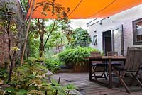 Decked patio with canopy and furniture. Sorbus cashmiriana, Hydrangea serrata 'Blue Bird', Hakonechloa macra. Tom de Witte garden.