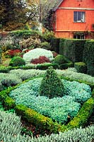 Formal herb garden with low buxus, diamond infilled with rue in walled garden, red painted house in background. Wyken Hall, Suffolk 