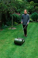 Woman mowing lawn using hand cylinder mower, June