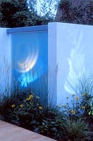 Modern town garden with dividing wall and frosted glass screen with coloured lighting, London.
