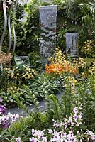 View from border to waterfalls mounted against a green wall. Planting includes Dendrobium 'Asian Youth Games Singapore 09' and Aranda 'Singa Gold'. The hidden beauty of Kranji. RHS Chelsea Flower Show, 2015