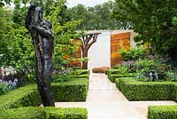 The Morgan Stanley Healthy Cities Garden. View of bronze sculpture and stone path with water feature leading to the wall covered with steel panels. Symmetric hedges of buxus sempervirens, fern - Dryopteris affinis, Salvia nemorosa 'Caradonna', Camassia cusickii and Lupinus 'Masterpiece'. 