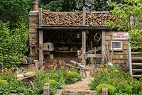 A Trugmaker's Garden, showing a traditional timber workshop edged in vibrant planting of poppies, geums, anchusa, cirsium and astrantia. 
