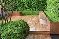 Bench at end of garden with rill and water-spout. Buxus sempervirens hedge and stems of Viburnum rhytidophyllum