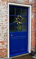 A festive wreath made from Holly, Ivy, Mistletoe and Pine cones hanging on a blue door