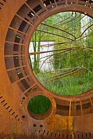 A rusted corten steel oculus and warped steel rods depicting the trajectory of light flow through the garden planted with foliage plants including Phyllostachys and grasses. Dark Matter Garden for the National Schools' Observatory. Design. RHS Chelsea Flower Show. 