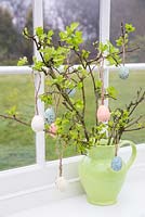Floral display containing fresh spring foliage and decorative eggs, with a view to the garden