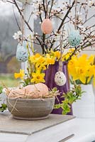 Floral display containing decorative eggs, Daffodils and blossoming spring foliage, with a view to the garden