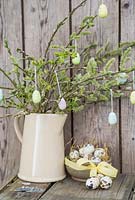 Decorative eggs hanging from fresh spring foliage, accompanied with a bowl of Quail eggs