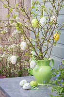 Decorative eggs hanging from fresh spring foliage in a green jug