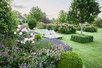 Formal garden with lawn and herbaceous borders planted with Geranium 'Patricia', Erysimum 'Bowles Mauve', lavender and Rosa 'Mortimer Sackler'.
