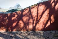 The ruin. Tree shadows on painted wave form wall. Veddw House Garden, Monmouthshire, South Wales. March 2015. Garden designed and created by Charles Hawes and Anne Wareham