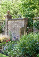 Border next to wall with gate, Allium, Paeonia, Geranium - Ammerdown House, Somerset