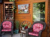 Seating area shelves and artwork on veranda of wooden cabin style house. Containr planting includes, Epipremnum sp, MIscanthus sinensis 'Gracillimus', Sempervivum, Senecio, Schlumbergera 