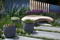Sculptured bench, striped paving interspersed with herb stripes, and pots of herbs in Living Landscapes: Healing Urban Garden at RHS Hampton Court Palace Flower Show 2015