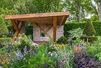 The oak and limestone loggia surrounded with Craig Shaffer sculpture by perennial sunny planting with Campanula 'Telham Beauty', Cirsium rivulare 'Atropurpureum' and Pinus 'Nana' in  The Morgan Stanley Garden - RHS Chelsea Flower Show 2017