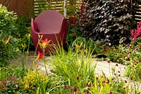 Wooden decking with chair and mixed flower borders with Fagus sylvatica, Sanguisorba officinalis 'Morning Select', Astilbe x arendsii Fanal', Bergenia and Hemerocallis 'Lusty Lealand' in Foundations for Growth at  RHS Hampton Court Palace Flower Show 2015.  