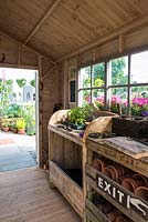 Just Retirement: A Garden For Every Retiree, view of shed interior with wooden potting bench and worktable with herbs, tools, pots and propagation equipment in a shed. Designer: Tracy Foster Sponsor: Just Retirement Ltd