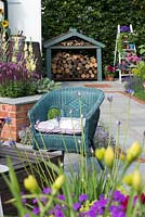 Just Retirement: A Garden For Every Retiree, view of blue painted wicker armchair and wood store. Designer: Tracy Foster Sponsor: Just Retirement Ltd