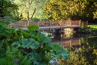 Footbridge over the lake on the edge of the garden. Himalayan Garden, Harewood House, Yorkshire, UK. Early Summer, June 2015.