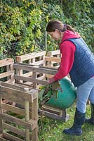 Woman adding garden waste to a Three Bin Composting system constructed from Upcycled wooden pallets