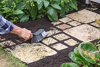 Using a hand brush to fill gaps in a path with soil