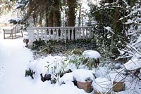 Winter scene with balustrade, wooden bench, plants in pots covered with leafes and snow - Welsch Garden, Berlin, Germany