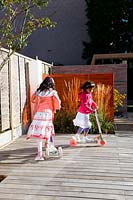 Small urban contemporary town garden children kids playing on decked patio terrace.  Ansari garden, Harrow
