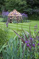 View from border containing Penstemon, Iris germanica and Phormium 'Bronze Baby', looking towards the unique Gabion sculpture shaped like a bulb