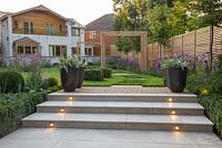 Marble steps with lighting feature at dusk with view to the house. Border of Verbena bonariensis, Buxus sempervirens hedge and spheres, Veronica and Calamagrostis x acutiflora 'Karl Foerster'. Potted Astelia chathamica