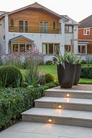 Marble steps with lighting feature at dusk with view to the house. Border of Verbena bonariensis, Buxus sempervirens hedge and spheres, Veronica and Calamagrostis x acutiflora 'Karl Foerster'. Potted Astelia chathamica