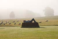 The main lawn in mist with bronze and corten steel sculpture by Sean Henry.  Sheep grazing in field beyond. 