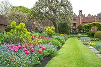 Chenies Manor Gardens, Buckinghamshire, showing the 'Sunken Garden' and House in Spring. Planting includes Tulipa 'Queen of Marvel', Myosotis, Hosta, Euphorbia, Primula 