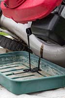 Tilt the lawn mower on its side and begin to drain the dirty engine oil into the empty tray