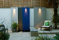Small urban courtyard garden with painted feature wall panels and water feature with downlighting, seating, changes of level, hard landscaping and low maintenance planting 