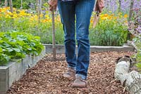 Woman walking down path of bark chippings mulch carrying garden tools